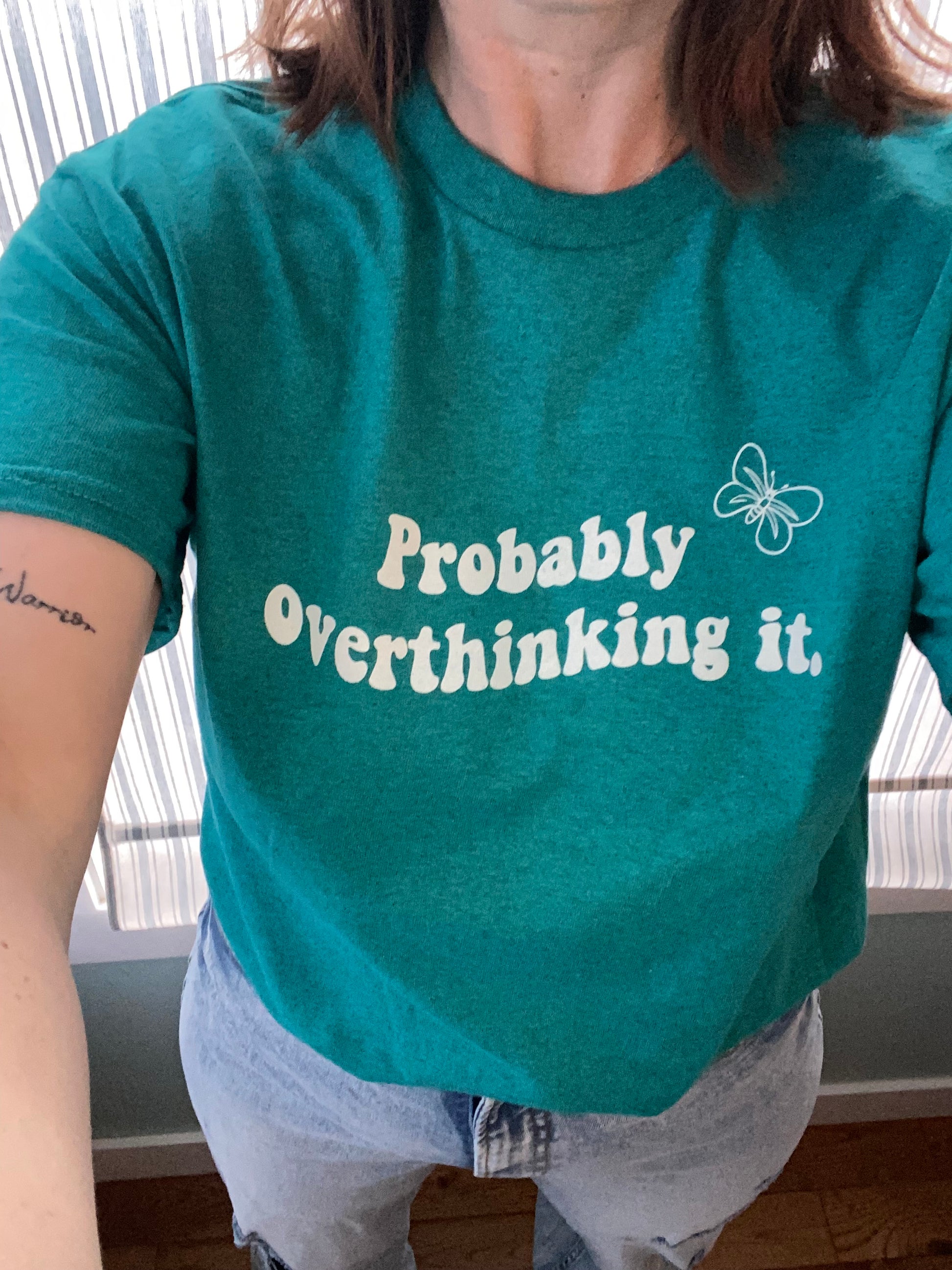 Probably overthinking it tee, in white writing with a butterfly also in white, in the top left corner. Wave design in the print, colour is in antique sapphire. Design is centered in the upper middle of the tee.  Loose fitting soft material, woman is taking a selfie from the neck down. 