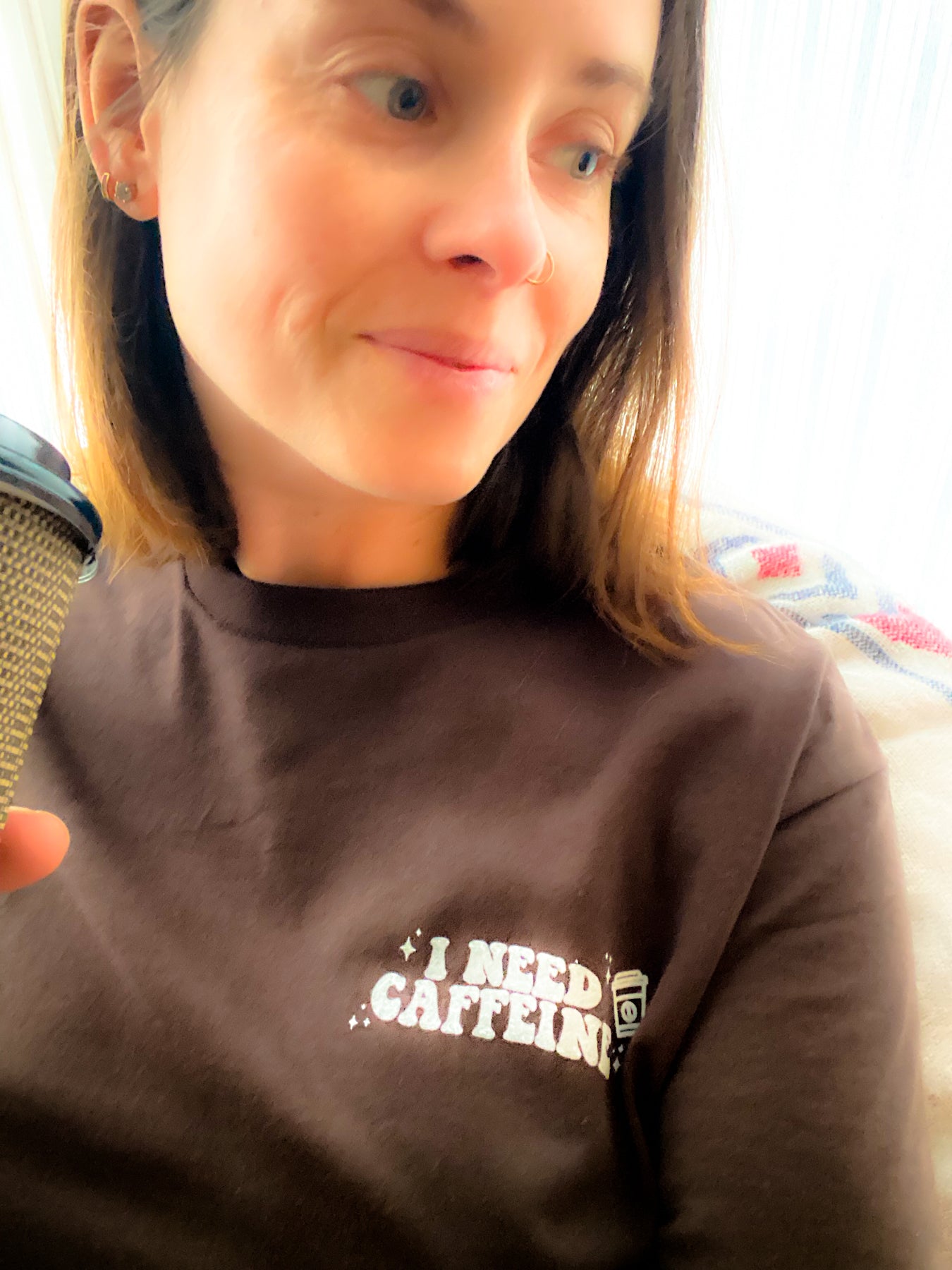 Close up of model Wearing "I NEED CAFFEINE" tee. Woman is holding a take out coffee cup that is also brown. She is looking away from the camera. The tee is in the colour chocolate. it is lightweight and soft. "I NEED CAFFEINE" is in an all white print with a small take out coffee cup beside it and also some small stars in each corner. The design is located on the upper left side of the t-shirt.