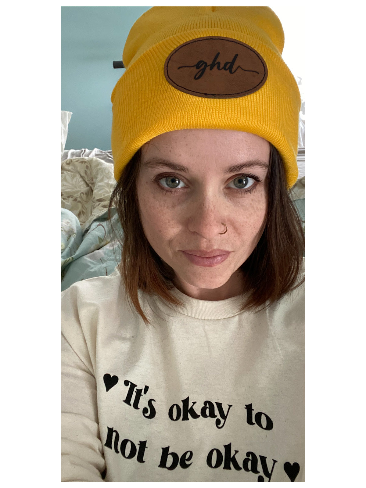 close up of a woman wearing the gold coloured ghd beanie. She is also wearing the "its okay to not be okay" long sleeved tee. 