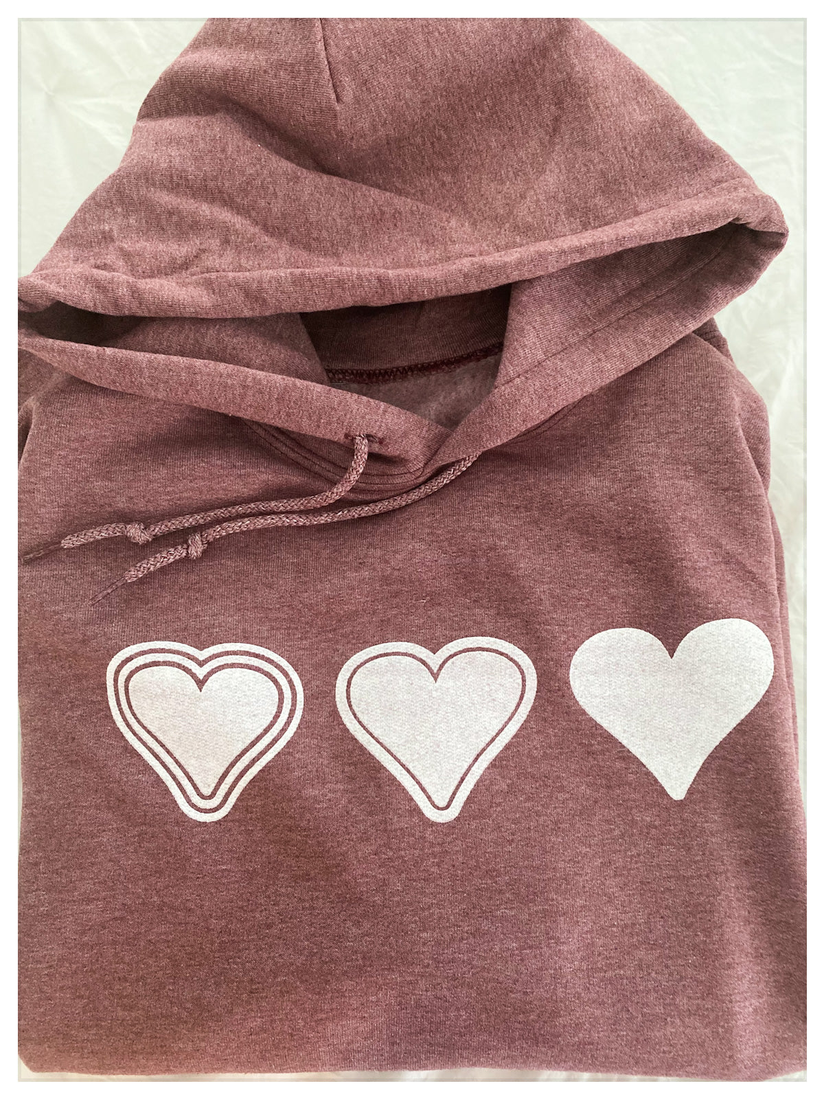 close up view of folded soft maroon sweatshirt, with three white hearts on it.