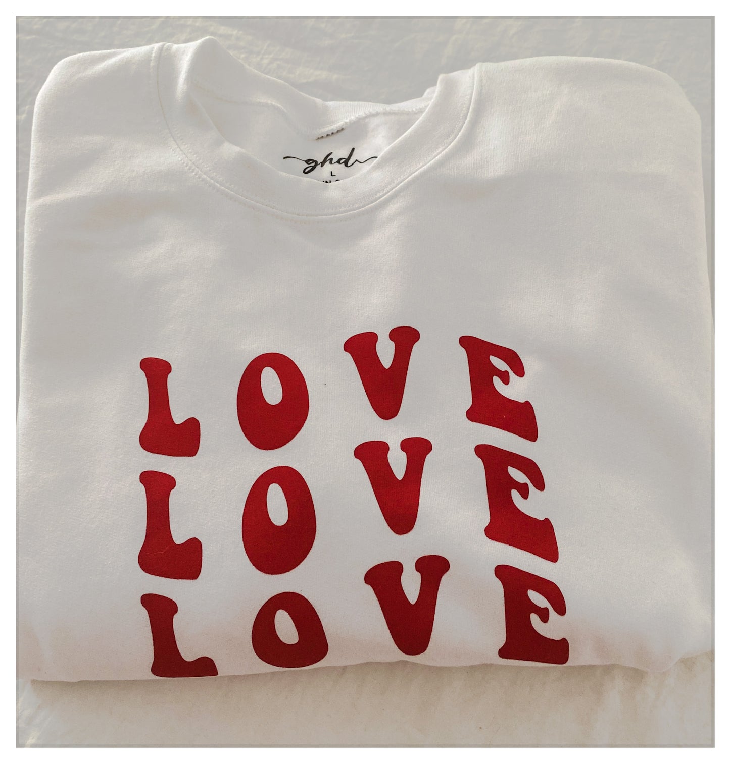 Close up folded cozy white crew, with "LOVE, LOVE, LOVE," printed in red coloured ink. 