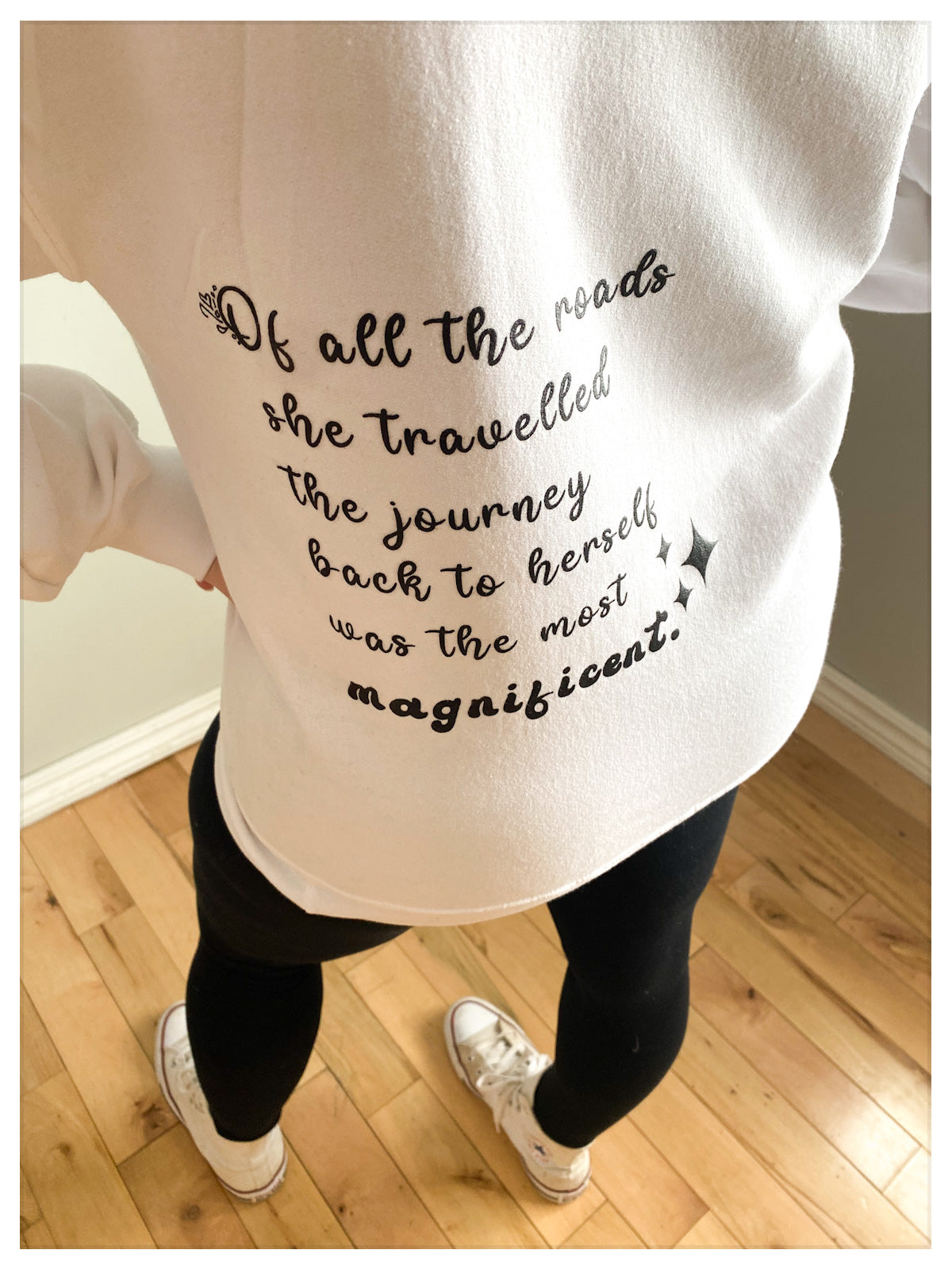 Close up of a white fleeced hoodie that says "Of all the roads she travelled the journey back to herself was the most magnificent." Written on the back left hand side, in black cursive print. 