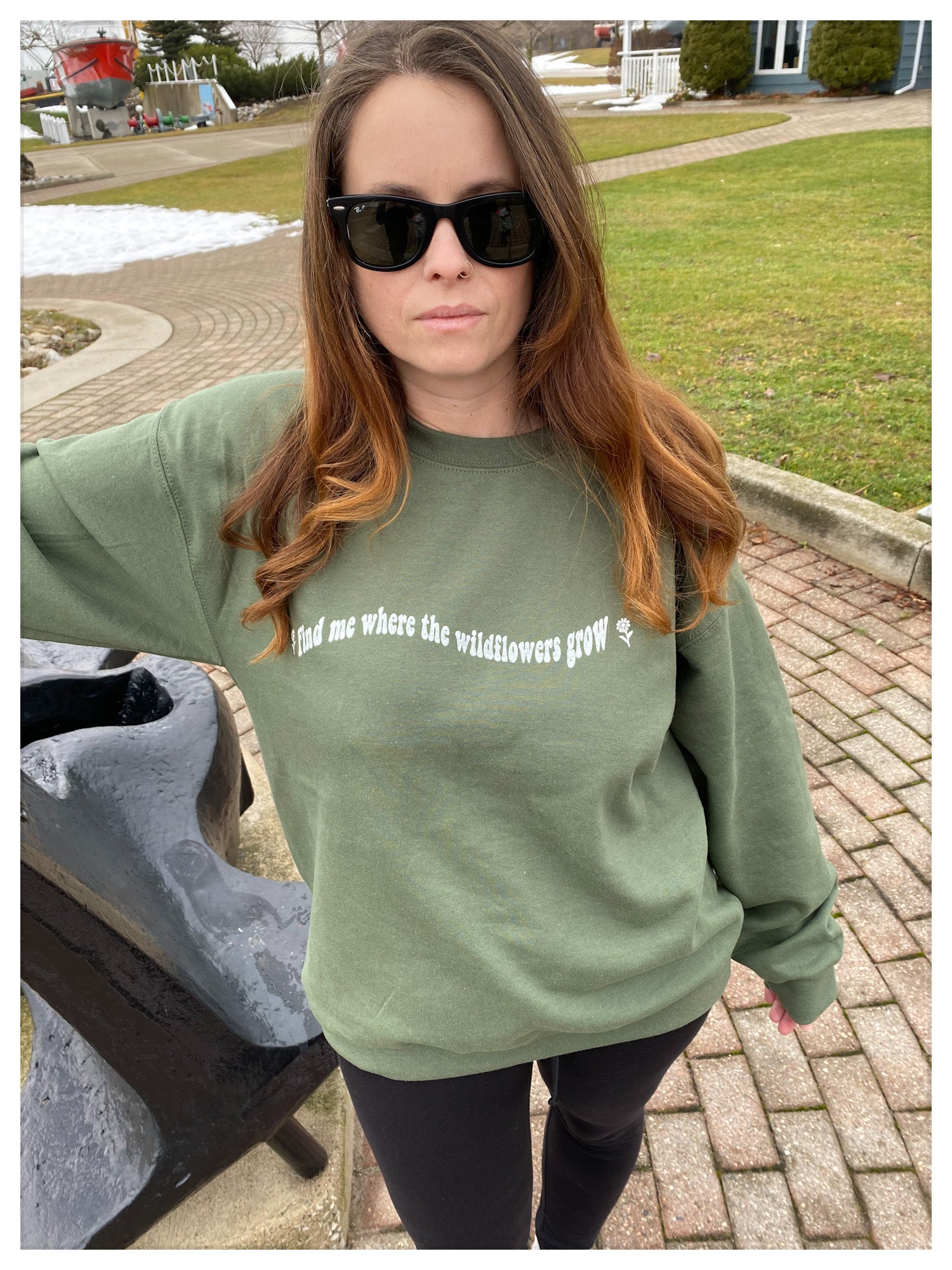 Girl wearing a casual army green sweater that says "Find me where the wildflowers grow"