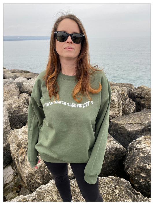 Girl standing on rocks wearing an army green warm casual crew "Find me where the wildflowers grow"